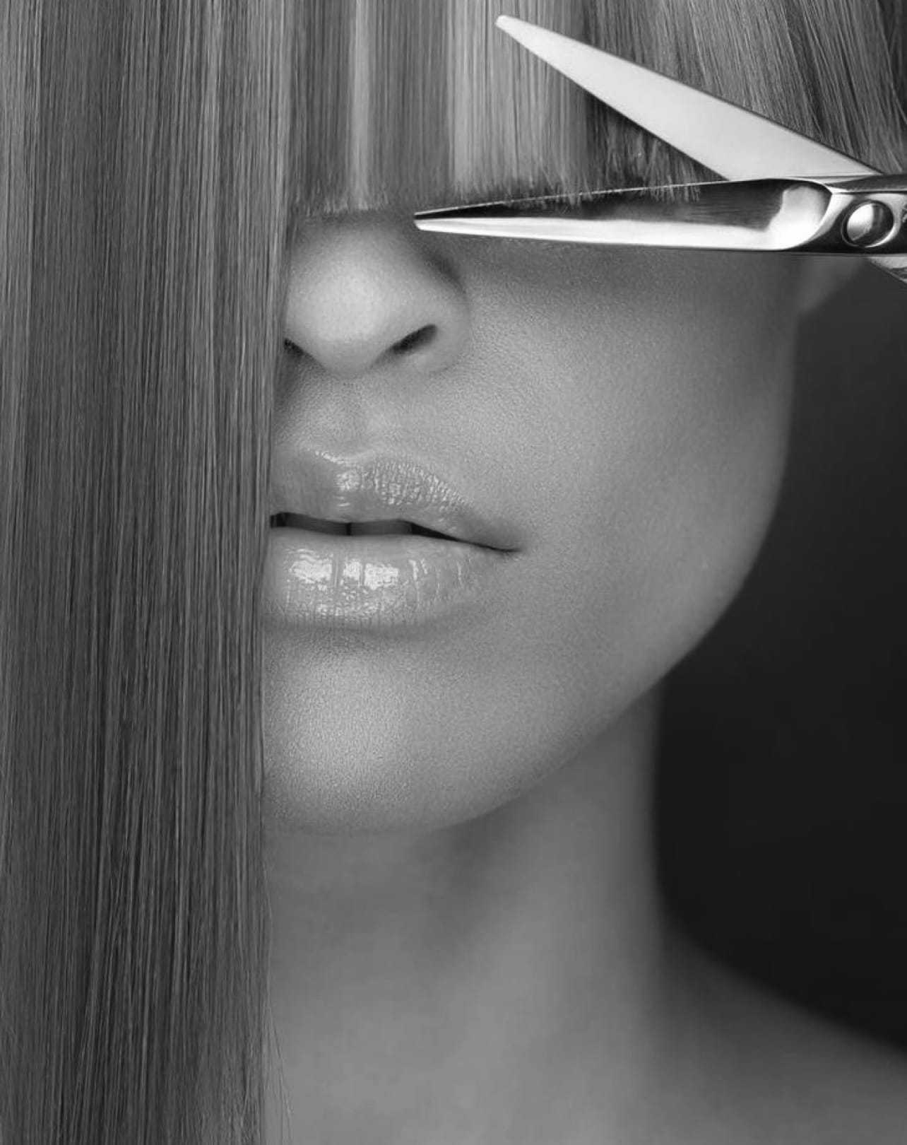 Haircut close-up: Scissors cutting straight bangs over closed eyes, emphasizing precision.