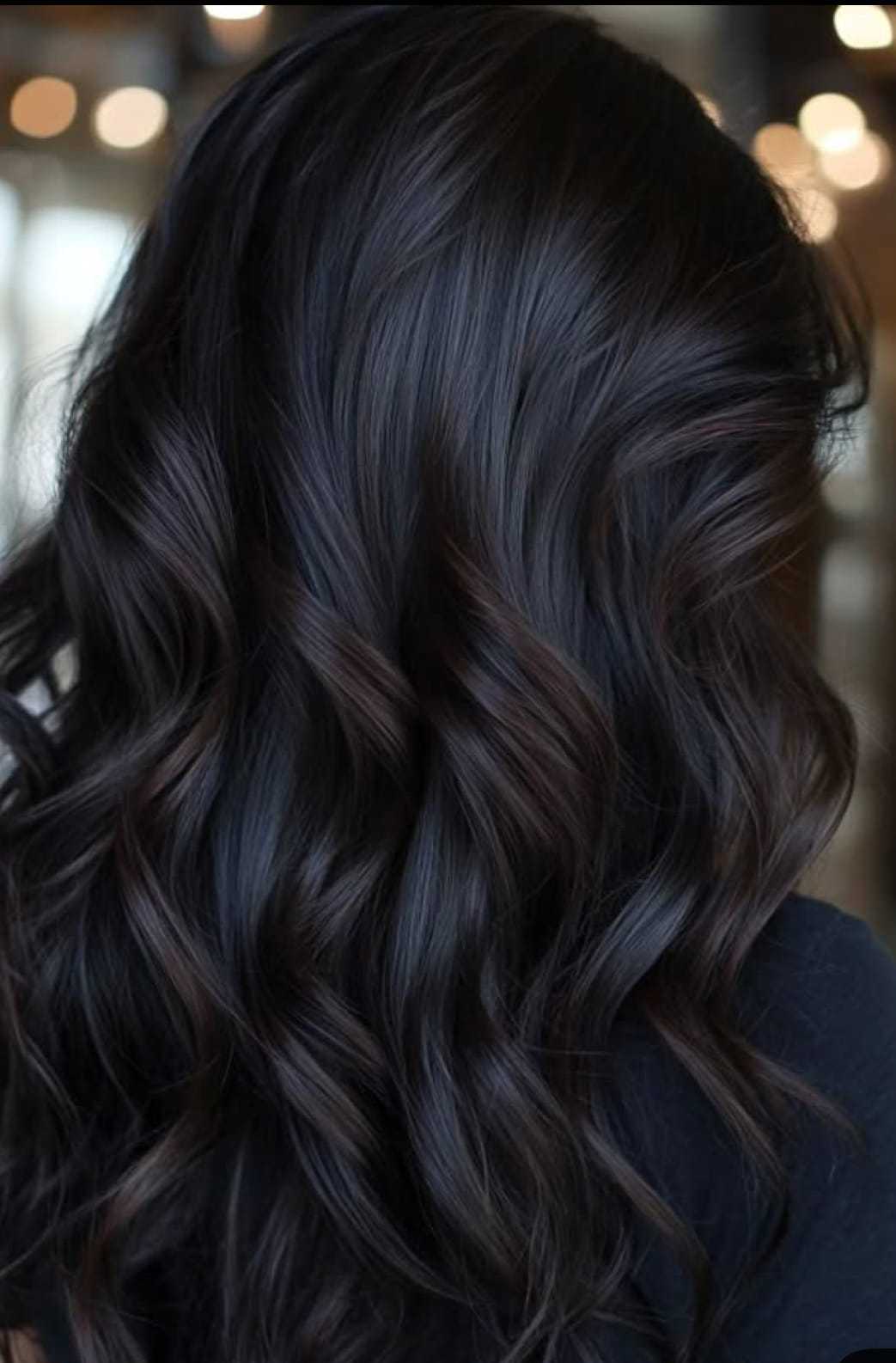 Rich, wavy black hair with soft curls, reflecting light, fills the frame.
