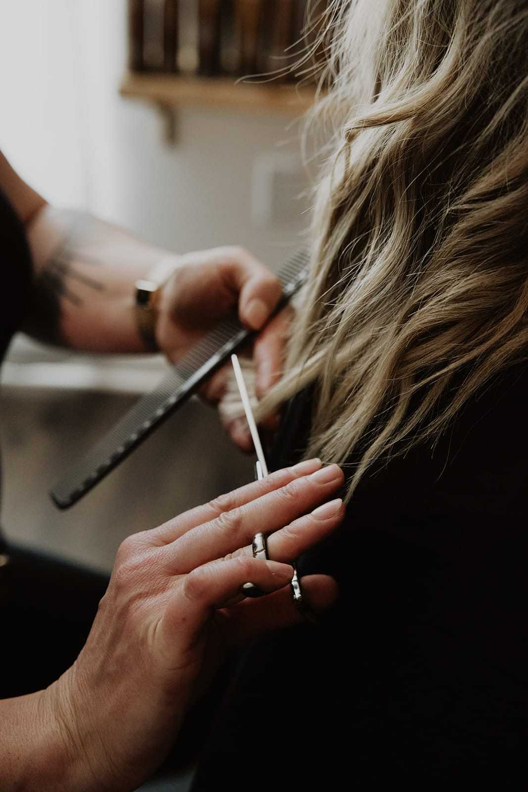 Hairdresser cutting a woman's wavy blonde hair with scissors in a salon.