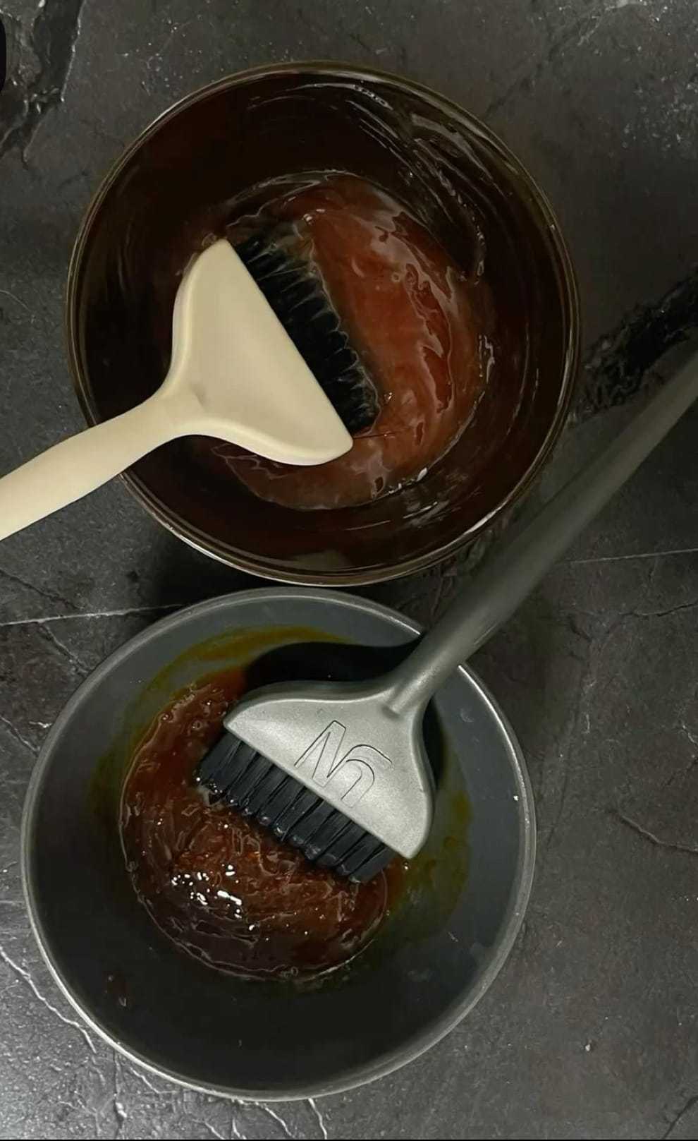 Hair dye brushes and bowls on a dark surface with hair color mixture.