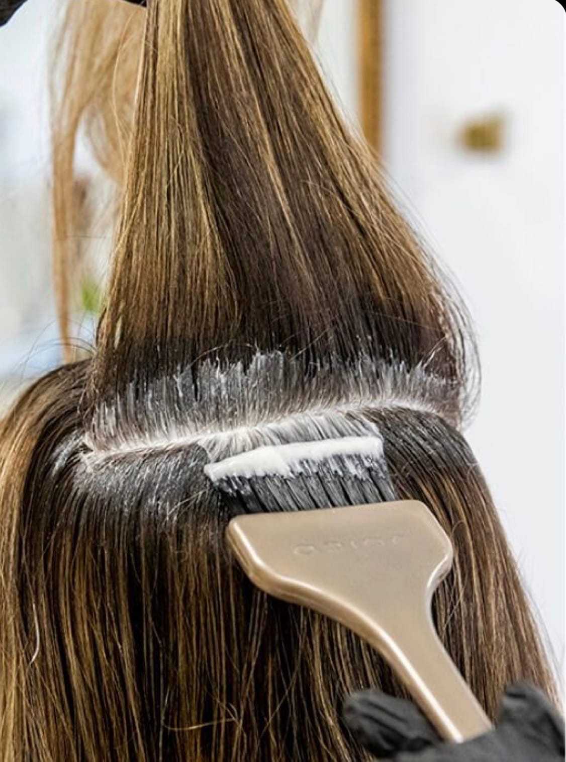 Hair dye being applied to roots with a brush in a salon.